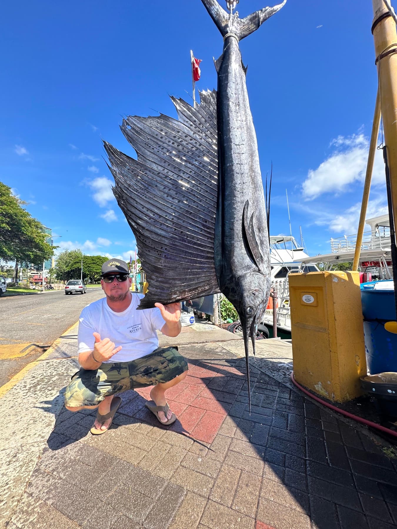 Capt. Rubin crouched beside a sailfish hanging at the Kewalo Basin dock