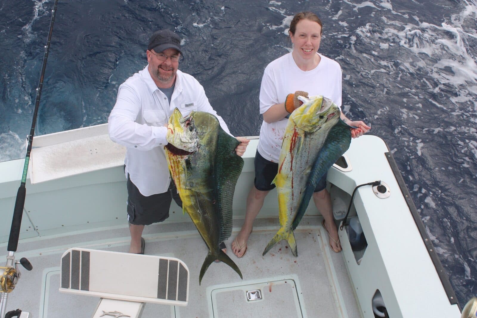 Two anglers holding bull mahimahi in the cockpit