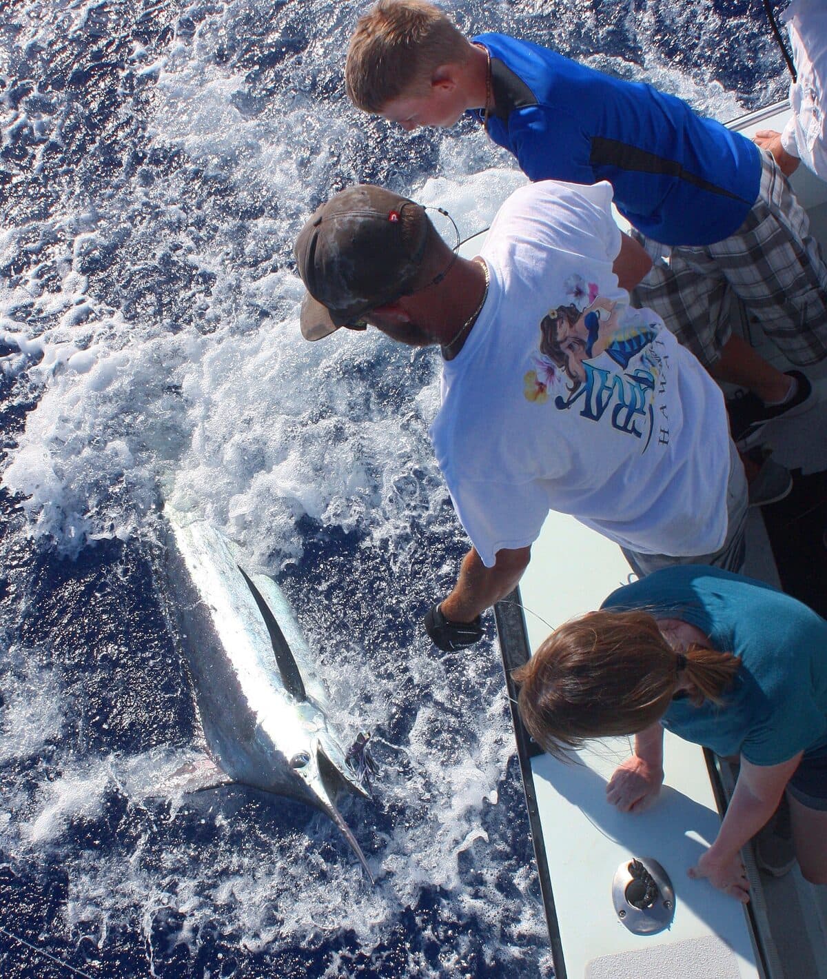A family watching the crew bring a marlin alongside the boat