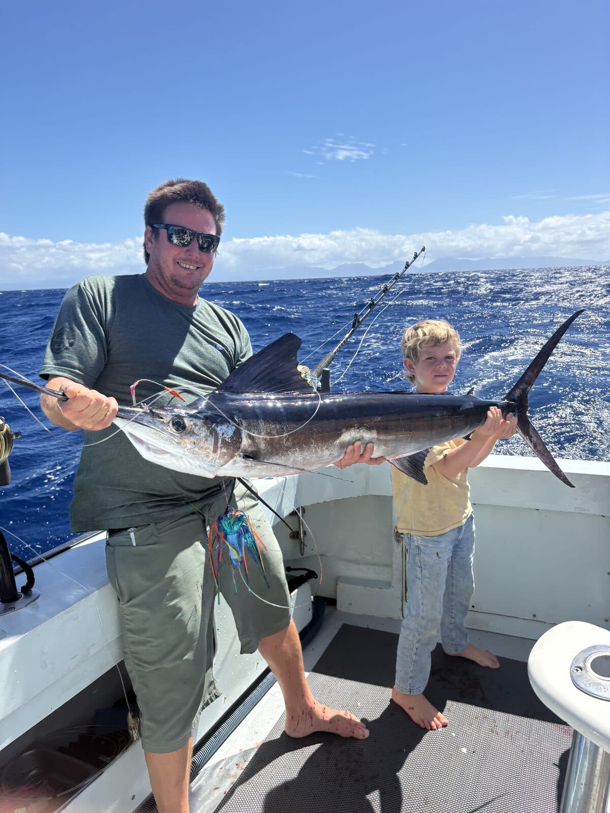 An angler and two kids holding a marlin aboard Ruckus