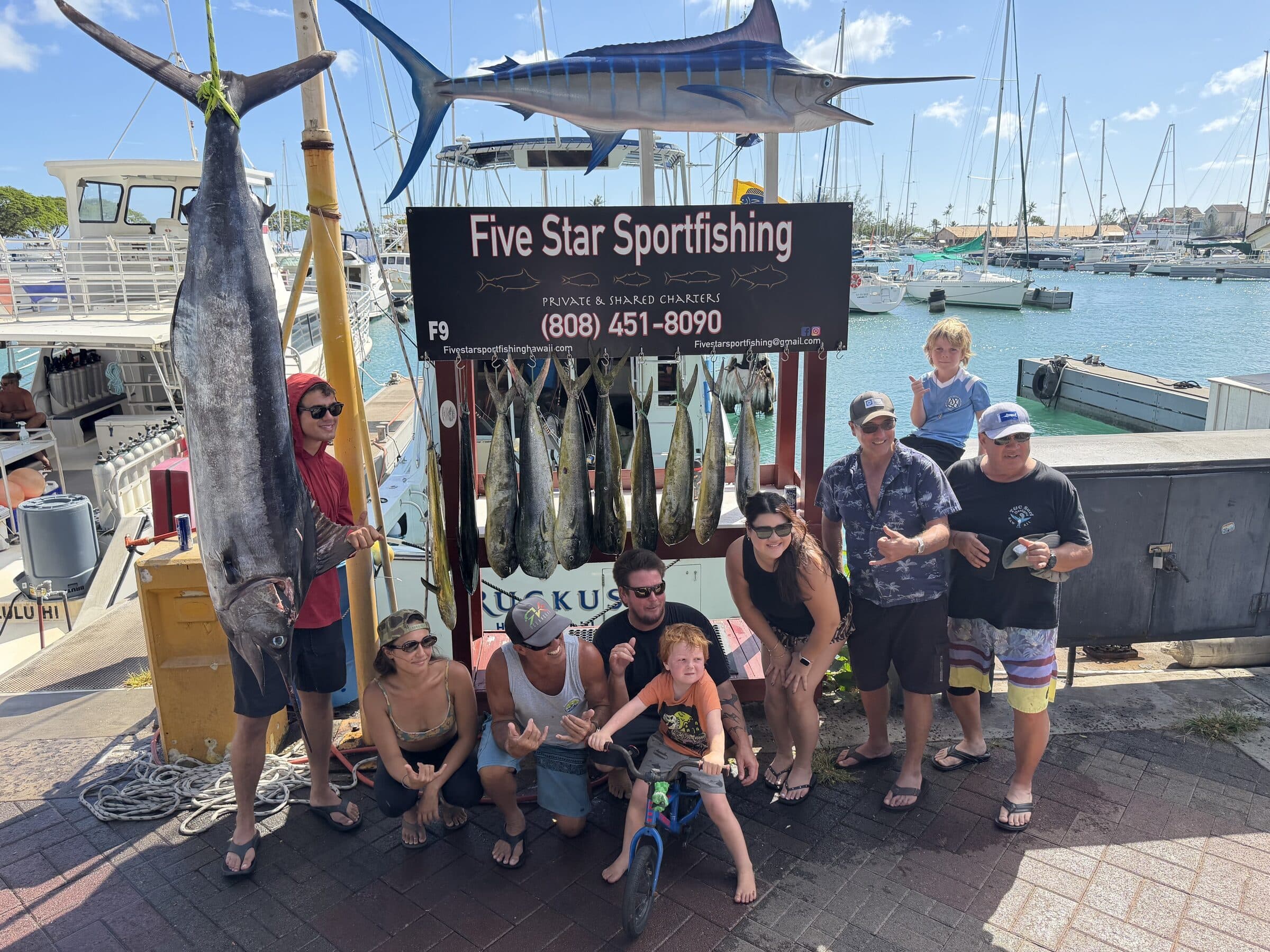 A blue marlin hanging under the Five Star Sportfishing sign with the whole crew and family